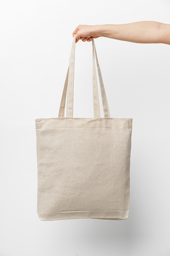 Female hand holding eco or reusable shopping bag against white background, close up
