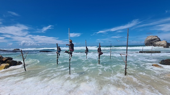 Koggala, Sri Lanka – April 30, 2022: Stilt fishermen fishing on a stick on the coast of Koggala, Sri Lanka.