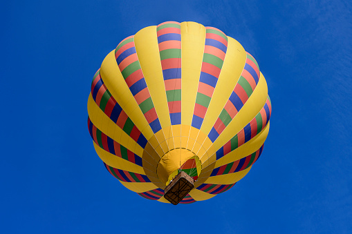 Colorful hot air balloon flying over green field and river