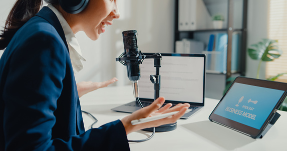 Close up of young Asian businesswoman recording and broadcasting a podcast on her laptop from studio office. Live streaming and broadcasting online concept.