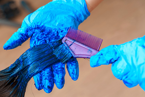 Gloved hands apply blue dye to hair with a comb.