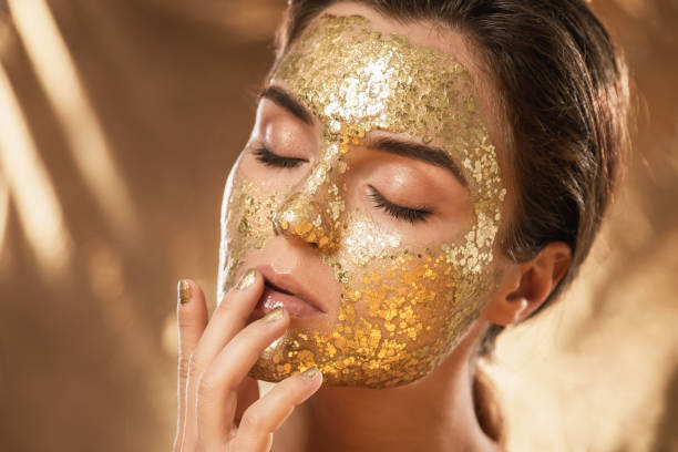 Beautiful woman with golden shining mask on her face for skin treatment Beautiful young woman with golden shining mask on her face for skin treatment Gold Facial Kit for skin stock pictures, royalty-free photos & images