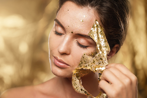 Beautiful young woman with golden shining mask on her face for skin treatment