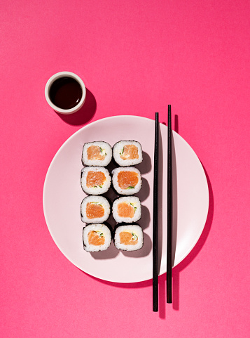 Japanese Sushi roll with salmon, cucumber and soy sauce with chopsticks in the plate on pink background with hard shadow. Concept food photography. Top view and copy space.