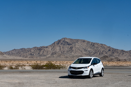 In the Sheephole Valley Wilderness, United States a Chevy Bolt Electric Vehicle is parked in the BLM desert area in front of a mountain on a sunny spring day.