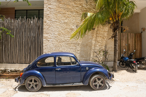 In Tulum, Mexico a classic, blue Volkswagen Beetle is parked outside on a residential street on a sunny summer day.