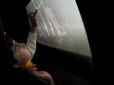 A child draws a heart with his finger on the fogged glass