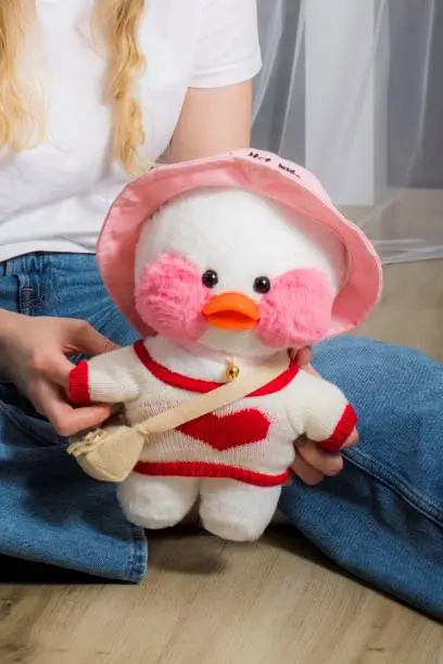 Photo of a little girl holds a popular duckling with pink cheeks, a soft plush duck with glasses