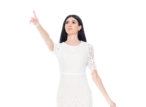 Waist up of aged 20-29 years old who is beautiful caucasian female standing in front of white background wearing dress who is smiling and touching who is pointing