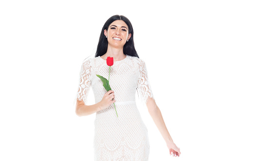 Waist up of aged 20-29 years old who is tall person with long hair caucasian young women standing in front of white background wearing dress who is happy and holding flower