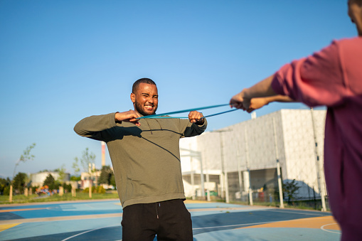 Young man doing exercises with rubber band with her partner outdoors