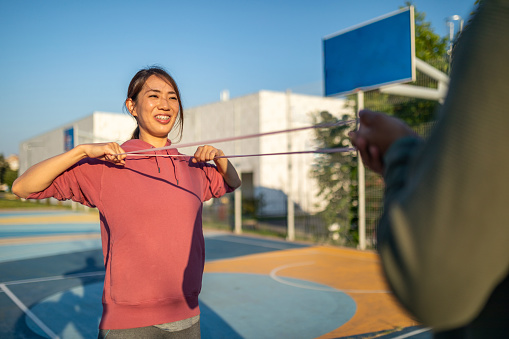 Young woman doing exercises with rubber band with her partner outdoors
