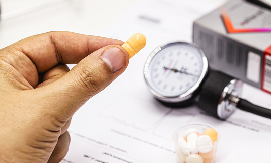 hand holding high blood pressure medication, pill or pill, medical tests and sphygmomanometer in the background