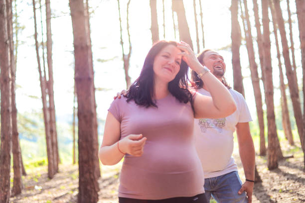 Stock photography of a young couple expecting a baby taking a walk into the forest on a sunny day