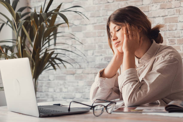 istock Young woman student sitting at desk full with books textbooks looking at computer screen to unfinished homework feels tired bored and unmotivated, girl loaded with tasks, work backlog overflow concept 1401810801