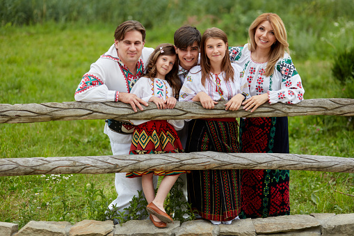 Happy family with kids in traditional romanian dress in a countryside, park. Father, mother, son and daughters walking outside.