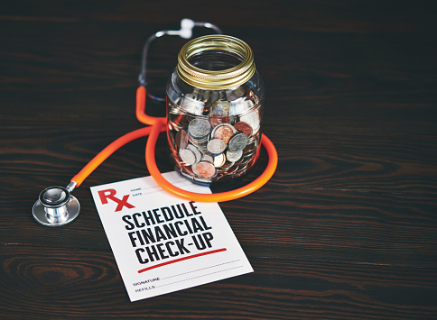 Money jar filled with coins with a stethoscope and a prescription for a financial check-up