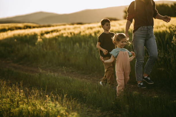 Mother with her little daughter and son walking on a meadow outdoors in sunset.