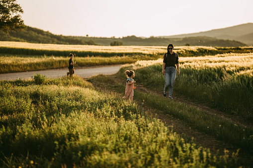 Mother with her little daughter and son walking on a meadow outdoors in nature.