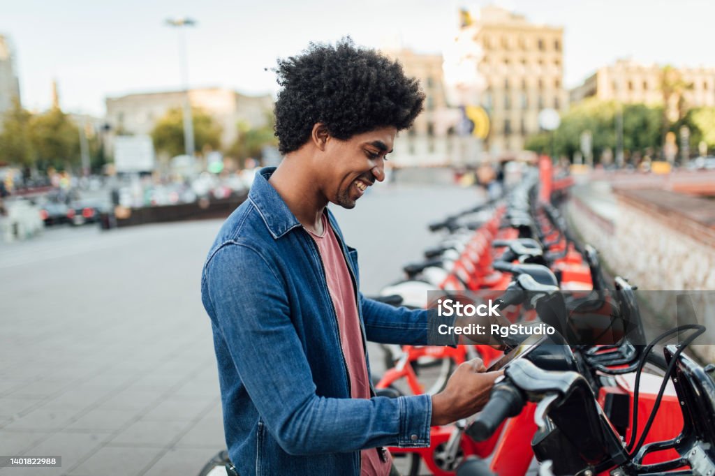 Portrait of a young Afro tourist renting an e-bike. Young African American tourist renting an e-bike to explore Barcelona. Bicycle Sharing System Stock Photo
