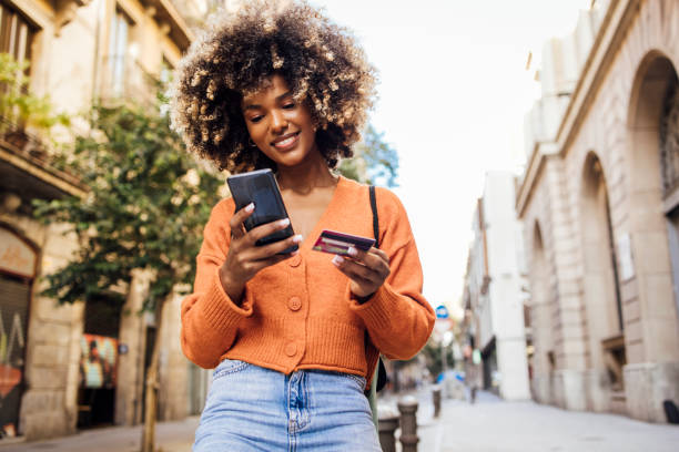Happy Afro girl in Barcelona shopping online on the move Portrait of a young African American woman on vacation in Barcelona shopping online on the street. credit card purchase stock pictures, royalty-free photos & images