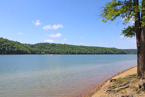 Sunny autumn afternoon at a lake in Springfield, Missouri, USA. Rocky edge to the lake surrounds the calm water. Sky is blue with a few white clouds.