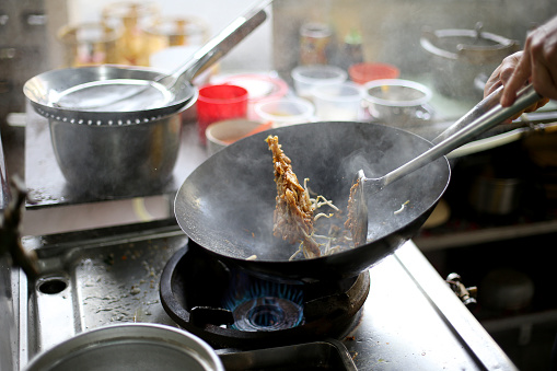 An Asian chef is cooking fried noodle in Chinese restaurant kitchen.