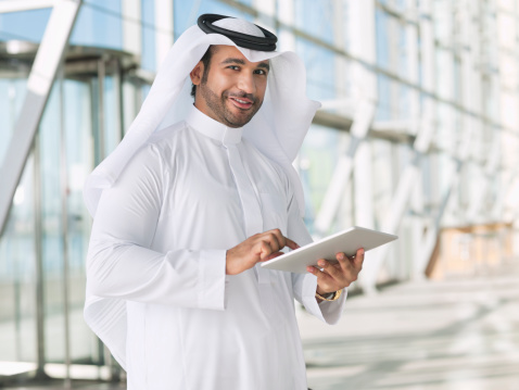 Retrato de la sonriente hombre de negocios usando tableta digital en tocado árabe photo