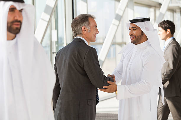 uomo d'affari in tuta agitare le mani con un uomo d'affari in kefiah - middle eastern ethnicity business greeting handshake foto e immagini stock