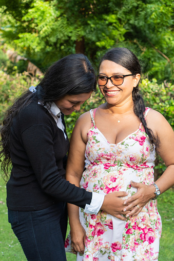 Latin daughter holds her mother's hands on her pregnant belly.