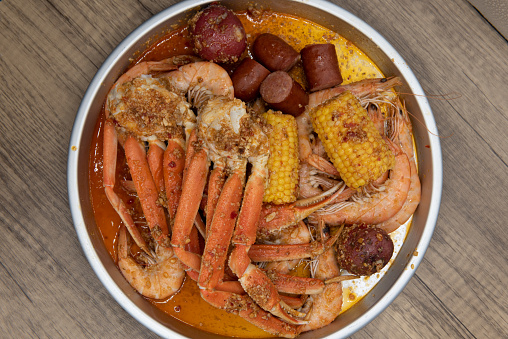 Overhead view of delicious buttery plate of boiled snow crab legs with corn on the cob and sausage for a tasty seafood meal.