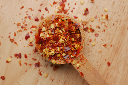 red chili pepper flakes in wooden spoon .