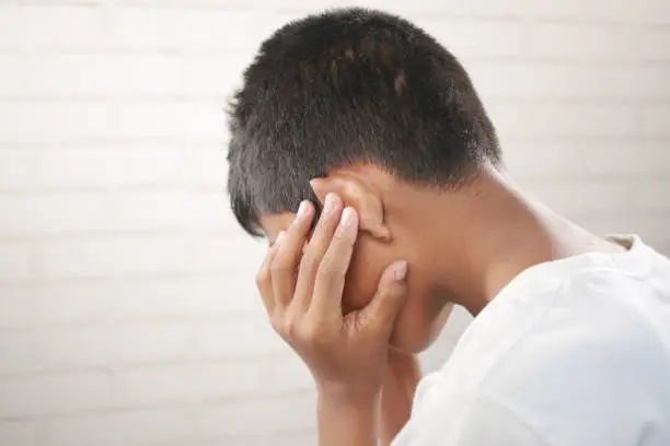 Photo of teenage boy having ear pain touching his painful ear ,