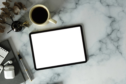 Flat lay digital tablet with empty screen, coffee cup and supplies on marble background.