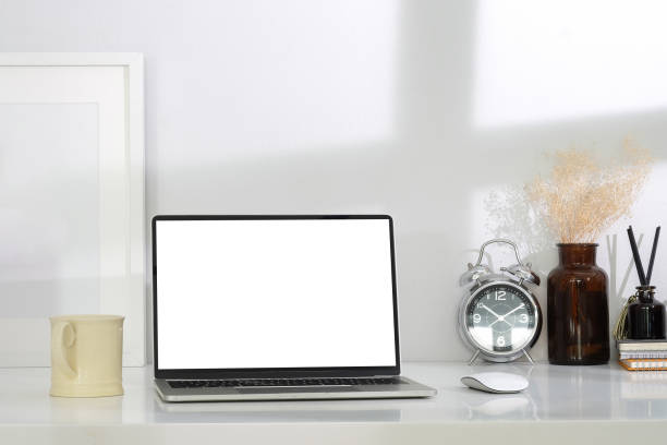 istock Mockup laptop computer, coffee cup, picture frame and supplies on white table in bright living room. Home office. 1401845825