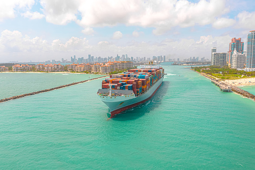 Moving container ship caught in action from this drone point of view with amazing turquoise blue waters, beaches, modern architecture, and more in frame