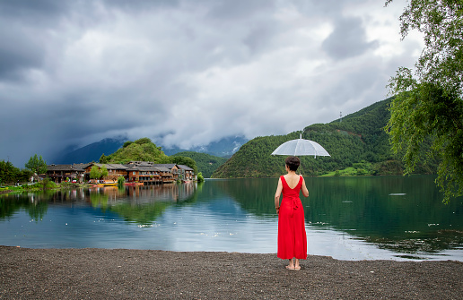 A woman in a red dress stands beside a lake dotted with white flowers at Lugu Lake in Lijiang, Yunnan Province, China