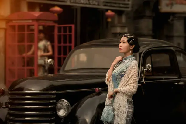 A woman in a qipao stands next to an old car, retro color card style