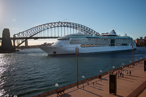 Australia, Sydney, 2019, April : Large cruise ship in front of the Harbour Bridge over the bay and the embankment