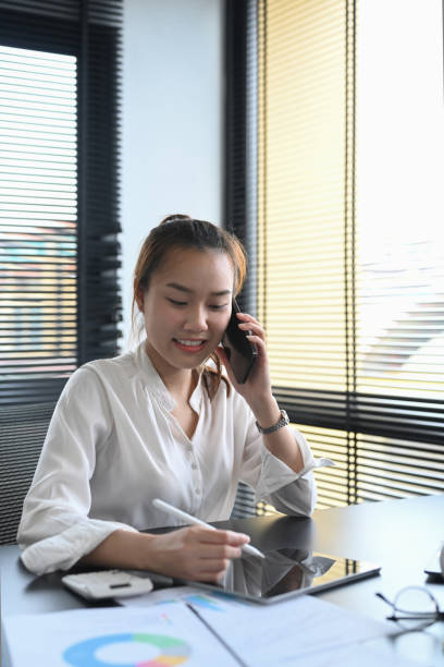 istock Young female financial advisor having phone conversation with client and using digital tablet at her workplace. 1401872931