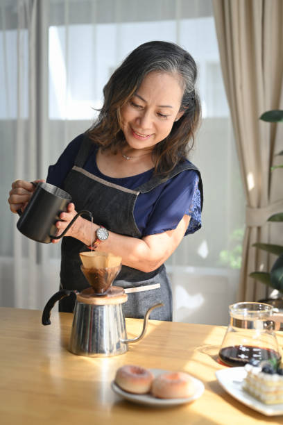 istock Smiling middle aged standing at kitchen table, brewing drip coffee and enjoys her morning. 1401872952