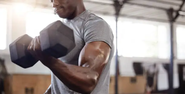 Photo of Unknown african american athlete lifting dumbbell during bicep curl arm workout in gym. Strong, fit, active black man training with weight in health and sports club. Weightlifting exercise routine