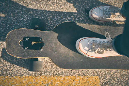 Feet of woman in sneakers on a double kick cutaway longboard in the city in the evening