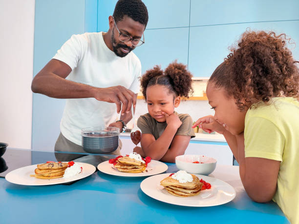 istock Black Father and Mixed-race Daughters Decorating Pancakes With Chocolate Together in the Morning 1401879123