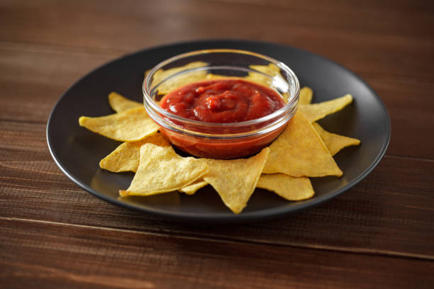 istock Nachos with tomato salsa on gray plate, on brown wooden table top, selective focus. 1401882225