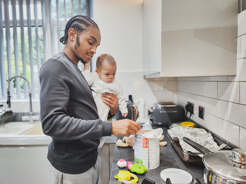 Candid portrait of a young black father and child preparing baby milk with formula powder at home in kitchen