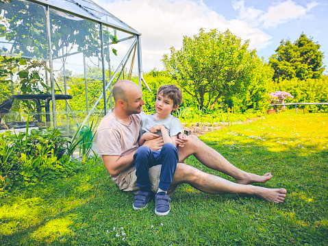 Father sitting in garden and enjoying a connection together with his disabled son. Physical contact and being outdoors can be both a challenge but also stimulating therapy for children with autisms.