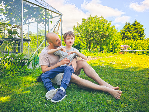 Father sitting in garden and enjoying a connection together with his disabled son. Physical contact and being outdoors can be both a challenge but also stimulating therapy for children with autisms.