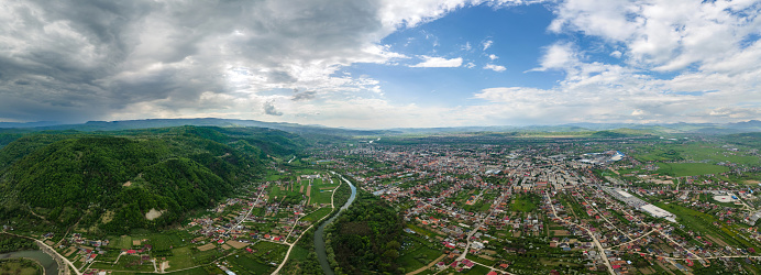 Aerial drone panoramic view of Sighetu Marmatiei, Romania. Town located in a valley with river and hills with green forest