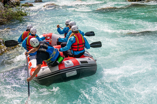 Rear view of friends wearing life jacket and rafting in river.